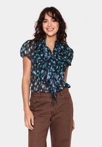 Črna bluzica z zelenim in modrim abstraktnim cvetličnim vzorcem, nabrano ovratnikom, kratkimi napihnjenimi rokavi in zavezanim detajlom okoli vratu. V kombinaciji z rjavimi hlačami.
