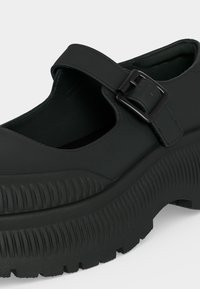 Chaussure Mary Jane noire et épaisse avec semelle texturée épaisse et bride réglable à boucle sur le dessus.