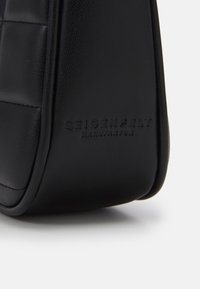 Angolo di una borsa in pelle nera con il nome del marchio in rilievo "Seidenfelt Manufaktur" visibile su una superficie liscia e texturizzata, su uno sfondo bianco.