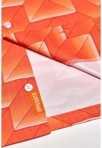 Oranžinės raštuotos medžiagos paviršius išsiskiria geometriniais raštais su tekstūra. Apima mygtukų detales ir etiketę su "OPPOSUITS" ženklu.