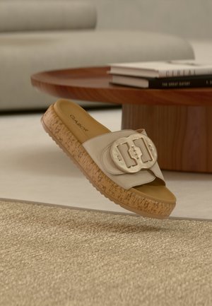 Sandale à glissière beige avec une large bride ornée d'une boucle de couleur dorée. Semelle plateforme à texture de liège avec une base en caoutchouc marron clair.