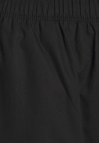 Musta kangas, jossa on kerrottu vyötärö, joka esittelee sileää tekstiiliä ja minimalistista muotoilua ilman näkyviä kuvioita tai yksityiskohtia.