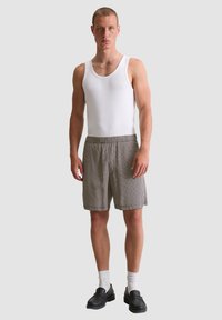 Witte tanktop, geruite shorts in grijs en zwart, platte schoenen en witte sokken. De outfit heeft een eenvoudige, ontspannen pasvorm en een casual stijl.