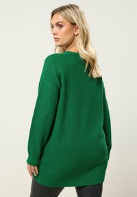 Zielony sweter dzianinowy o luźnym fasonie, z prążkowaną teksturą i długimi rękawami, z okrągłym dekoltem i nieco wydłużonym tyłem.