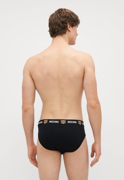 Črne bombažne hlačke z blagovno znamko na pasu, ki vsebujejo obliko medveda. Prilegajo se tesno in minimalistično ter imajo gladko teksturo.