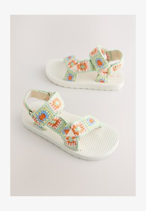 Zaļas un baltas sandales ar tamborētas stila siksnām, kurās ir oranži, zili un rozā ziedu raksti. Teksturēta balta zole.