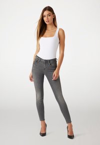 Fitted grå jeans med medelhög midja, fem fickor och lätt nöttning; kombinerat med en vit bodysuit och svarta spetsiga klackar.