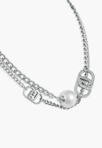 Srebrny łańcuszek z dwoma prostokątnymi metalowymi logo oraz jedną dużą białą perłą na jednolitym białym tle.