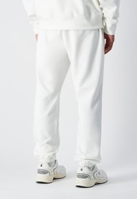 Pantalons de survêtement en coton blanc mélangé avec une taille élastique et des poignets. Assortis à des baskets de couleur claire avec des accents noirs et blancs.