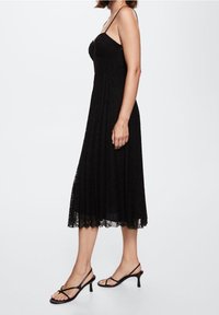 Černé krajkové šaty s kterými je korzet dobře padnoucí, nastavitelnými ramínky a rozšířenou sukní, která sahá do poloviny lýtek. V páru s černými sandály na tenkých podpatcích.