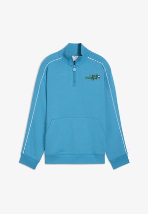 Svjetlomodra majica s četvrtastim zatvaračem, rebrastim ovratnikom, manžetama, prednjim džepom, bijelim obrubom uz rukave i malim zelenim vezenim krokodilom na prsima.