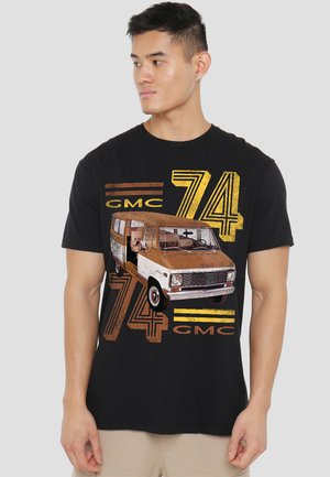 Schwarzes T-Shirt mit einem GMC-Truck-Grafik in erdigen Tönen, mit "74" und "GMC"-Text in gelben und braunen Streifen. Glattes Baumwollmaterial.