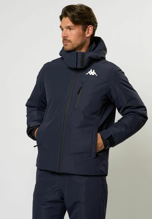 Marinblå isolerad jacka med hög krage, dragkedja fram och logodetalj. Inkluderar fickor och åtsittande ärmslut för värme och skydd.