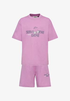 Dwoje dzieci ubranych w pasujące fioletowe koszulki "Serve the Game" i spodenki z białymi skarpetkami i niebieskimi trampkami, stojących na jednolitym tle.