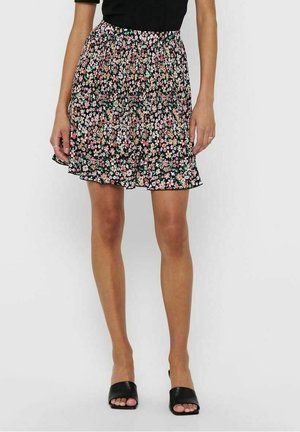 Mujer con falda negra de línea A con pequeñas flores rosas, blancas y verdes, combinada con zapatos negros abiertos en la punta tipo slide.