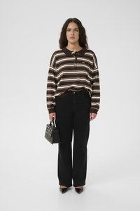 Woman standing wearing a brown and white striped long-sleeve polo shirt, black wide-leg pants, black pointed shoes, and holding a black handbag.