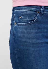Donkere blauwe denim jeans met een close-up weergave die de gladde textuur, lichte vervaging en een voorzak met een klein metalen accent toont.