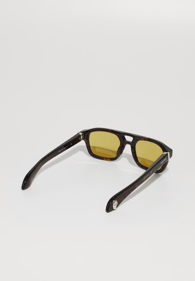 Ochelari de soare tortoise brown cu lentile galbene, formă pătrată și brațe negre elegante. Detalii metalice pe balamale adaugă un accent subtil.