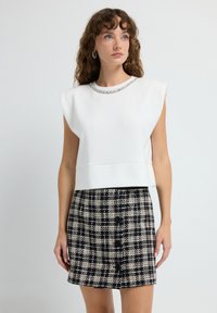 Top blanco sin mangas con escote texturizado y una falda corta a cuadros en blanco y negro que presenta botones frontales y un diseño estructurado.