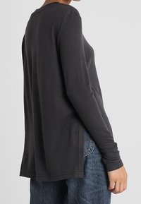 T-shirt a maniche lunghe e collo rotondo di colore grigio scuro, realizzato in morbido cotone, con una vestibilità rilassata e spacchi laterali per una maggiore libertà di movimento.