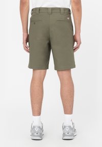 Pantaloni corti verde oliva con una texture liscia, dotati di tasche posteriori e passanti per cintura. Indossati con calze bianche e scarpe da ginnastica grigie.