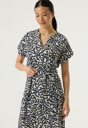 Kurzärmeliges Kleid aus weißem Stoff mit blauem, abstraktem Muster, V-Ausschnitt und einem gebundenen Gürtel, der die Taille betont. Strukturierte Oberfläche.