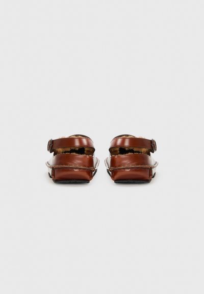 Sandales en cuir marron avec des sangles à boucle réglables, design ouvert à l'arrière et semelle intérieure texturée. Semelle plate avec détails de couture contrastants.