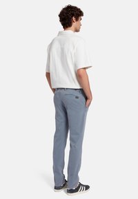 Witte overhemd met korte mouwen en een comfortabele pasvorm, gecombineerd met lichtblauwe broeken en donkere sneakers met witte strepen. Eenvoudig en casual ontwerp.