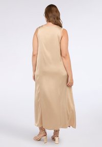 Beige satiini maksi dressi, jossa on rento istuvuus, hihaton malli ja pyöreä pääntie. Pituus ulottuu nilkkoihin, ja siinä on minimaalista yksityiskohtaisuutta ja sileä pinta.