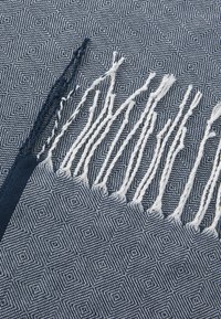Navy blue woven blanket featuring geometric patterns, fringed edges with alternating blue and white threads, and a textured finish.