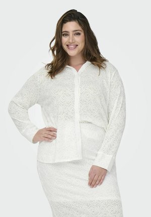 Blouse blanche à boutons, à manches longues, avec un motif en spirale texturé et une coupe décontractée. Tissu doux et léger avec une finition lisse.