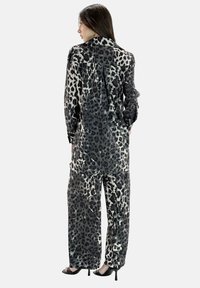 Ensemble chemise et pantalon imprimé léopard noir et gris, en tissu lisse. Présente des manches longues et une coupe ample.