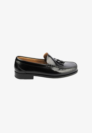 Mocasín de cuero negro con borlas y detalles cosidos, tacón bajo y forro interior color marrón claro, mostrado de lado sobre fondo blanco.