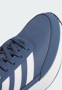 Niebieski but sportowy z teksturowaną cholewką, białymi paskami i ciemną gumową podeszwą. Posiada sznurowanie z przodu oraz wzmocniony nosek.