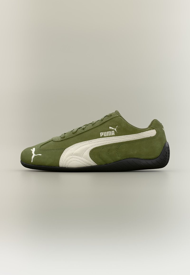 Αθλητικό παπούτσι Puma από καστόρι σε ελιά απόχρωση με λευκή γραμμή και λογότυπο, μαύρη σόλα, φωτισμένο από το πλάι σε ουδέτερο φόντο.