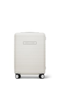 Hartschalenkoffer in mattem Weiß mit horizontalen Rillen, Tragegriff und vier schwarzen Rollen für Mobilität. An der Vorderseite befindet sich eine schmale Öffnung.