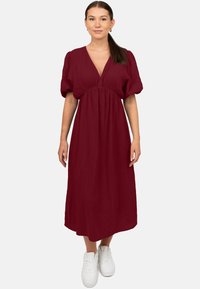 Bordeaux midi-jurk met een diepe V-hals, pofmouwen en een geraffineerde taille, gemaakt van textuurstof, gecombineerd met witte sneakers.