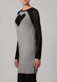 Robe pull en tricot gris avec des manches en filet noires et un motif en cœur sur le devant ; elle présente un ourlet et des poignets côtelés.