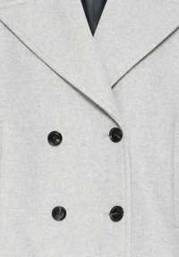 Manteau en laine gris clair à double boutonnage avec larges revers et quatre boutons noirs, laissant entrevoir une partie d'un vêtement intérieur noir.