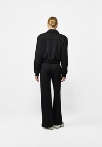 Czarna, dopasowana kurtka z kołnierzem i prążkowanym dołem w połączeniu z szerokimi czarnymi spodniami. Strój charakteryzuje się gładką fakturą i spójnym designem.