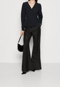 Černý top s obalem a texturou puntíků, dlouhými rukávy a detailem na zavázání, spárovaný s černými širokými kalhotami s vysokým pasem a texturou.