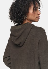 Sudadera con capucha de color marrón oscuro, con una textura suave, que presenta un corte oversized y ribetes acanalados en la capucha y el escote.