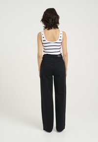 Svarta vida jeans och en vit tanktop med svarta ränder. Tanktoppen har djup rygg och jeansen har bakfickor och bälteshällor.