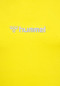 Gelbes Sportshirt mit geripptem Material und silbernem "hummel"-Logo. Der Stoff hat eine glatte Oberfläche und eine taillierte Passform.