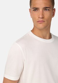 Biela tričko s krátkym rukávom z ľahkého materiálu s klasickým okrúhlym výstrihom a jemnými švovými detailmi na výstrihu a pleciach.