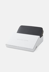 Portefeuille en cuir texturé noir partiellement visible dans une boîte blanche avec un logo argenté. La boîte a une forme rectangulaire et une finition lisse.