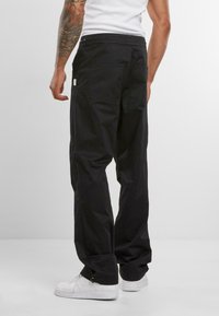 Black cargo pants made of cotton, featuring a relaxed fit, side pockets, and a drawstring waist. Paired with white sneakers.