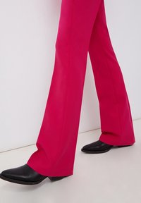 Fuchsiové kalhoty s rozšířenými nohavicemi vyrobené z hladkého materiálu, se zvýšeným pasem. Černé kotníkové boty s špičatou špičkou, jemnou texturou a nízkým podpatkem.