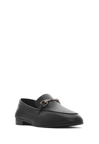 Mocassino in pelle nera con tacco basso e una decorativa catena in tonalità argento sul davanti. Texture liscia, forma affusolata.