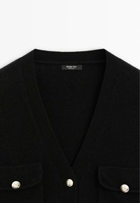 Cardigan in maglia nera con scollo a V, due tasche sul petto e dettagli in bottoni color oro. Texture morbida, design pulito e finitura moderna.